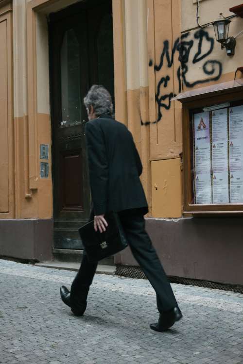 Person Walks Quickly With Bags By A Brown Building Photo