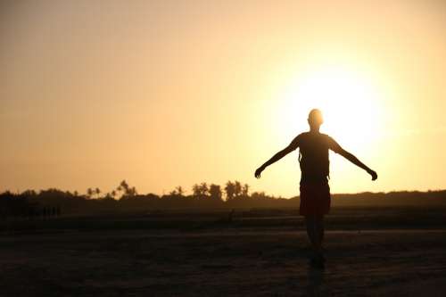 Person Holds Out Arms Silhouetted By A Setting Sun Photo