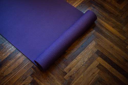 Purple Yoga Mat Partially Rolled On A Wooden Floor Photo