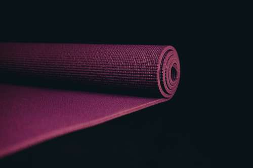 Purple Yoga Mat Partially Rolled Up On Black Photo