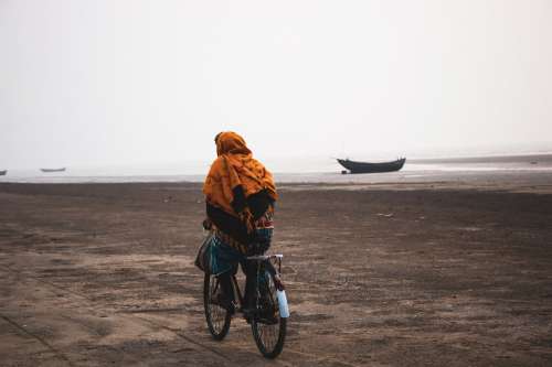 Person Wrapped In Orange Rides Their Bike On The Beach Photo