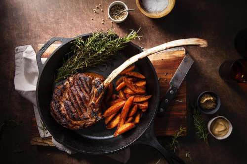 Iron Skillet With Meat And Potatoes On Wooden Board Photo