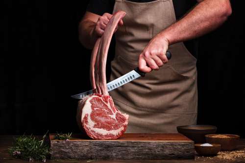 Person Holds A Sharp Knife Over Large Cut Of Meat Photo