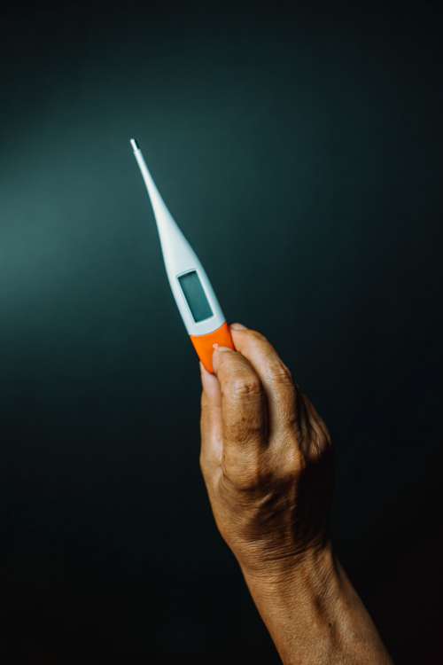 A Hand Holds Up A Thermometer Against Black Background Photo