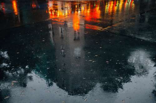 Wet Pavement Reflects A Building And City Night Lights Photo