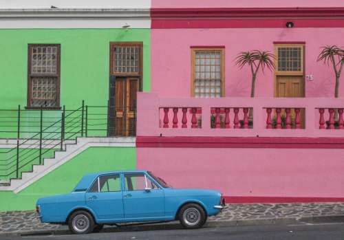 Blue Car Parked Next To A Green And Pink Building Photo