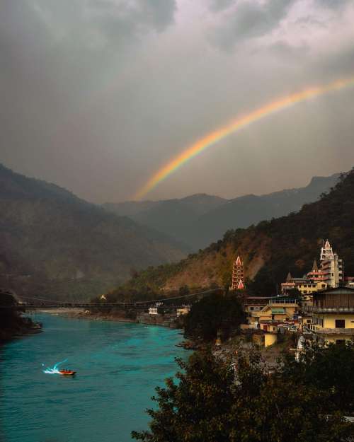 Blue River Between Two Hills With A Vivid Rainbow Arching Above Photo