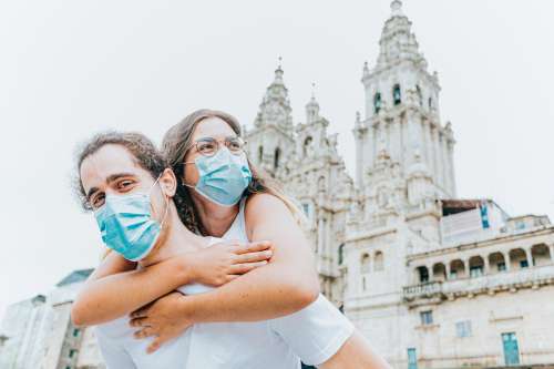 Woman Hugs Man From Behind While Wearing Blue Facemask Photo