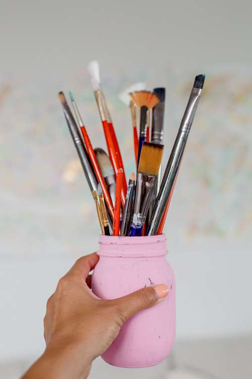 Hand Holds A Pink Mason Jar Filled With Paint Brushes Photo