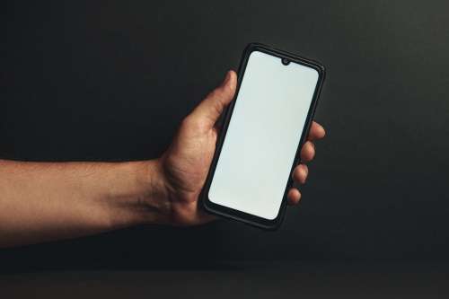 Hand Holds Out Phone Against Black Background Photo