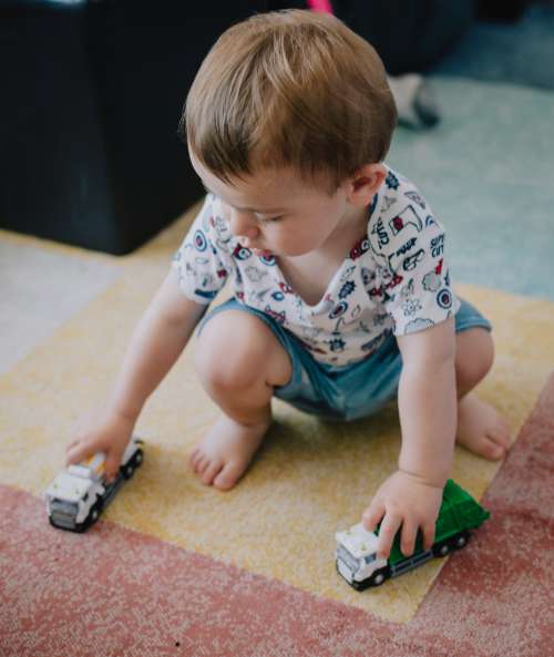 Small Child Squats And Plays With Toy Trucks Photo