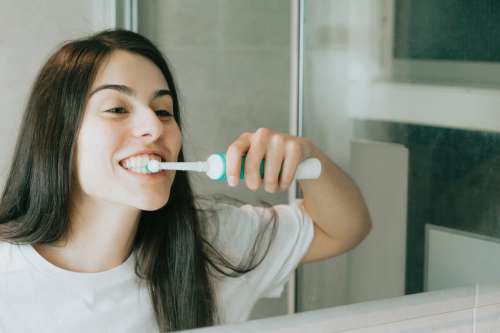 Woman Brushes With An Electric Toothbrush In A Mirror Photo