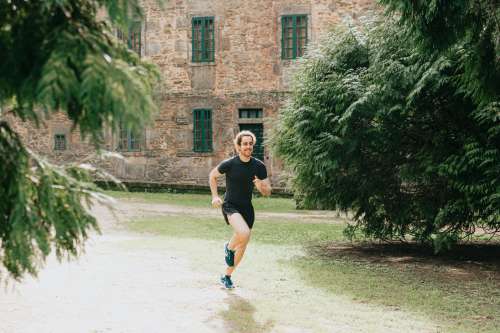 Man Runs Outdoors With A Stone Building Behind Him Photo