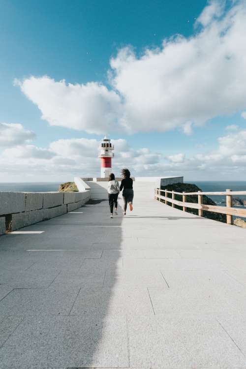 Two People Run Towards A Red And White Lighthouse Photo