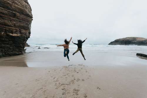 Two People Jump High On A Sandy Beach Photo