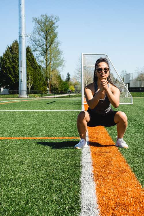 Woman Squats In Workout Gear On A Grassy Field Photo