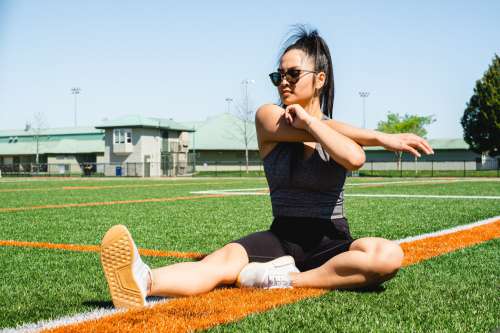Woman Sits On A Sports Fields And Stretches Her Arms Photo