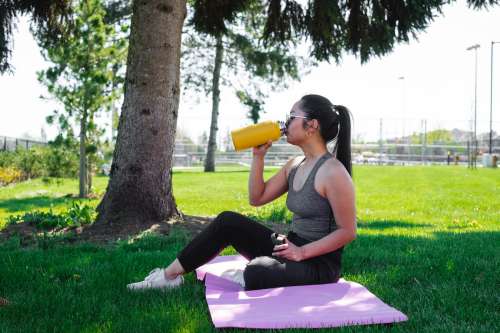 Woman Drinks From A Yellow Water Bottle Under A Tree Photo