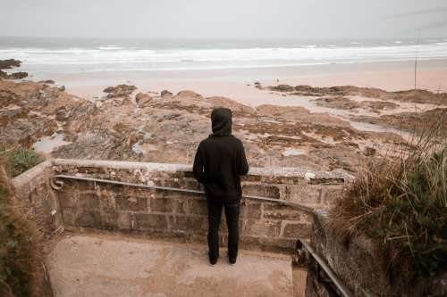 Person Dressed In Black Looks Out To A Sandy Beach Photo