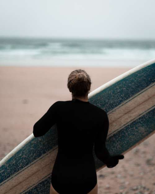 Person Carries Their Blue And White Surfboard To The Ocean Photo