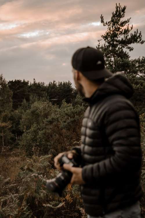 Person In Black Holding A Camera With The Forest Behind Photo