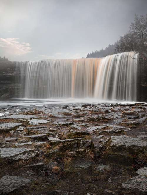 Long Exposure Of A Waterfall With Wet Brown Stones Photo