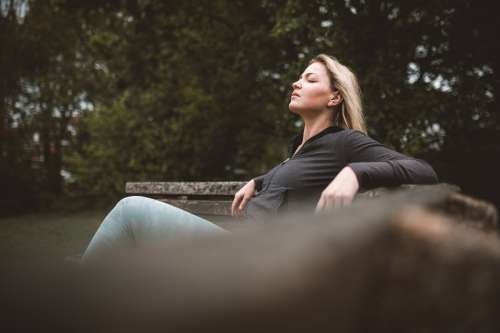 Woman Sits On A Bench Outdoors With Eyes Closed Photo