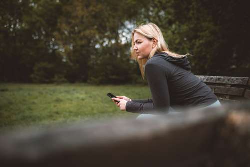 Woman Holds Her Cellphone And Sits On A Park Bench Photo