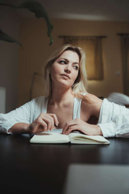 Woman Looks Up In Deep Thought As She Journals Photo