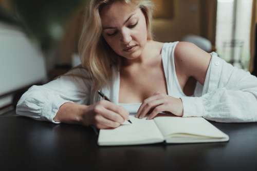 Woman Writes In Her Notebook Sitting Back At A Table Photo