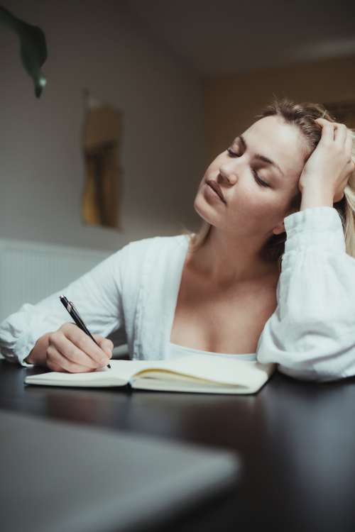 Woman Holds Her Head Thinking While Writing In A Journal Photo
