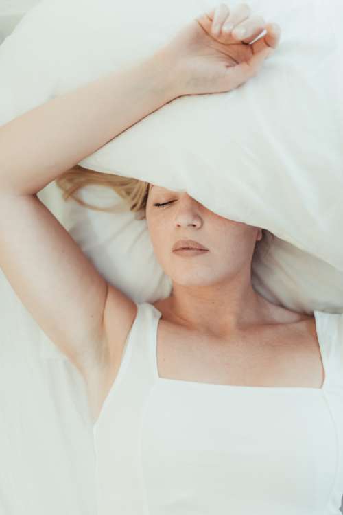 Woman Lays In A Bed With A Pillow Over Her Head Photo