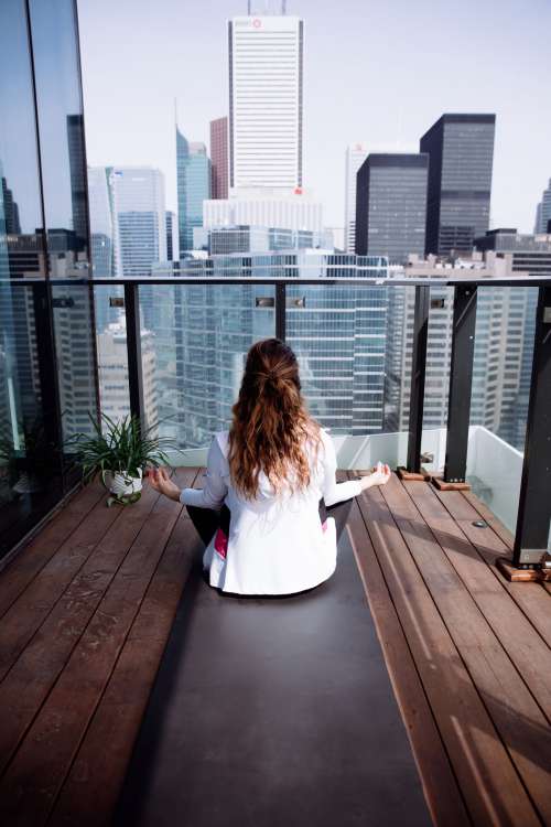 Person Faces The City While Sitting On A Yoga Mat On A Balcony Photo
