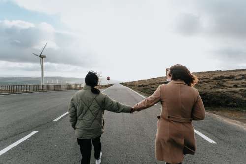 Two People Hold Hands And Walk Down A Paved Road Photo