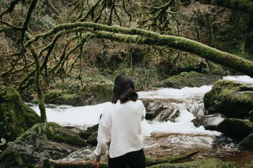 Person In White Sweater Stands Facing A Rushing River Photo