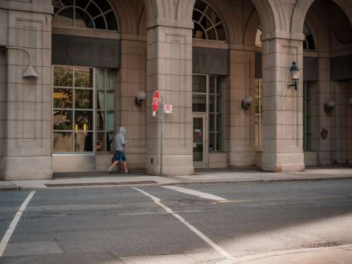 Person Walking Under A City Building With Tall Archways Photo