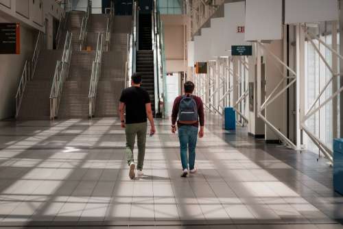 Two People Walk Towards Tall Stairs In An Atrium Photo