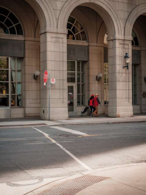 Two People In Red Walk Under A City Building Archway Photo