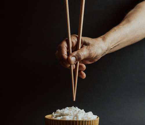 Hand Holds Chopsticks Over A Bowl Of Rice Photo