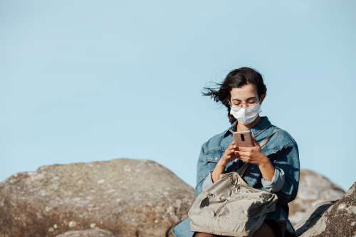 Person Looks Down At Their Cellphone While Sitting Outdoors Photo