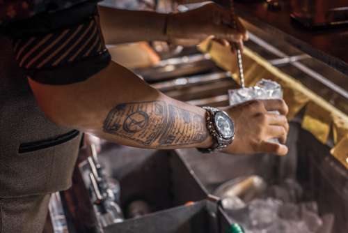 Tattooed Person Holding A Glass With Ice Over A Bar Well Photo