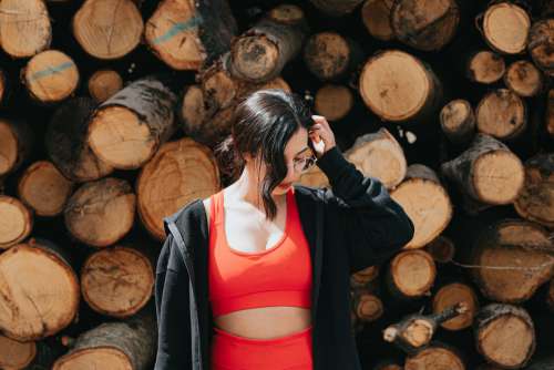 Woman In Red Athletic Wear Stands In Front Of A Stack Of Wood Photo