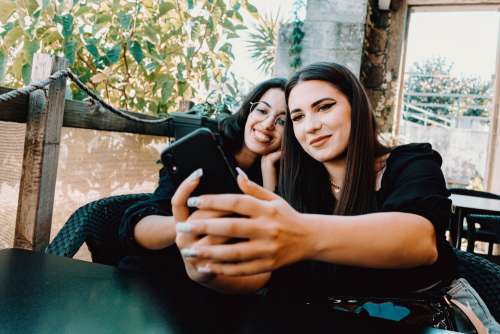 Two Women Lean Into Each Other And Take A Selfie Photo