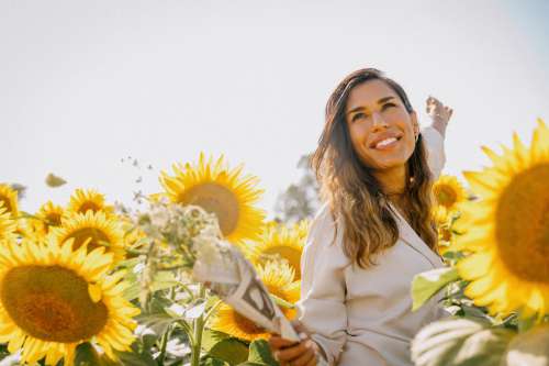 Woman In White Jacket Smiles Surrounded By Sunflowers Photo