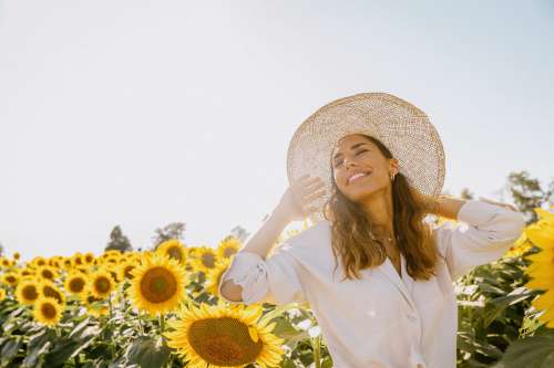 Woman Tilts Her Head Up Towards The Sun Holding Onto Hat Photo