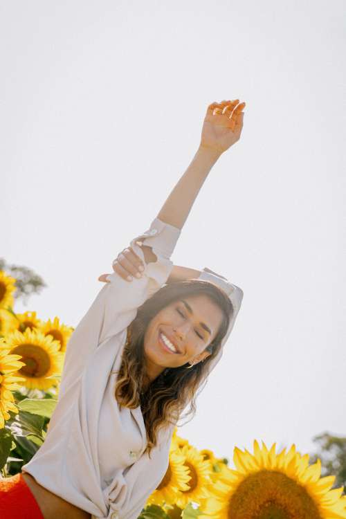 Woman Smiles With One Arm Up To The Sun In A Sunflower Field Photo