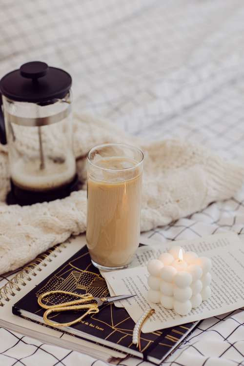 Glass Iced Coffee A Notebook And Lit Candle On A Bed Sheet Photo
