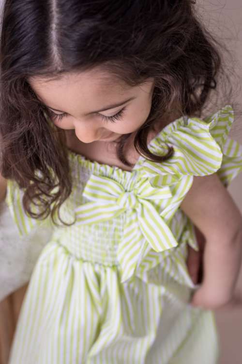 Young Child In A Green And White Dress Looks Down Photo