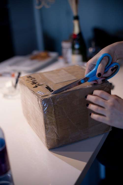 Person Uses Scissors To Cut Open A Taped Cardboard Box Photo
