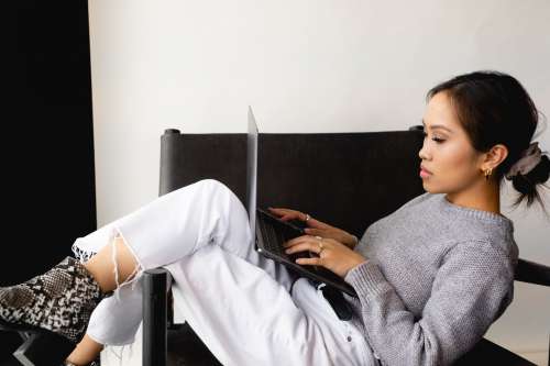 Woman Sits With Her Legs Up And Types On A Laptop Photo